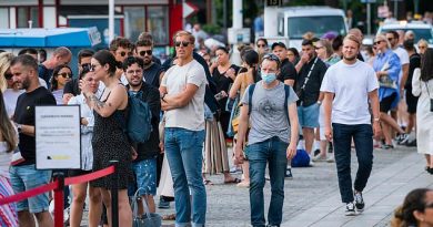 A man wearing a face mask walks past a line of people not wearing masks as they wait to board a boat at Stranvagen in Stockholm. Mask sales have soared in the past three weeks since the public health agency suggested they might be of benefit