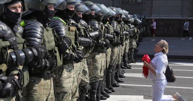 A Belarusian opposition supporter kneels in front of riot police officers during a protest in Independence Avenue in Minsk on Sunday