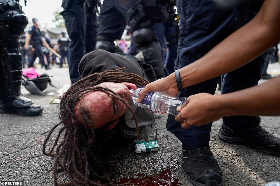 A protester offers water to a man as he is detained on the ground by police officers clad in riot gear