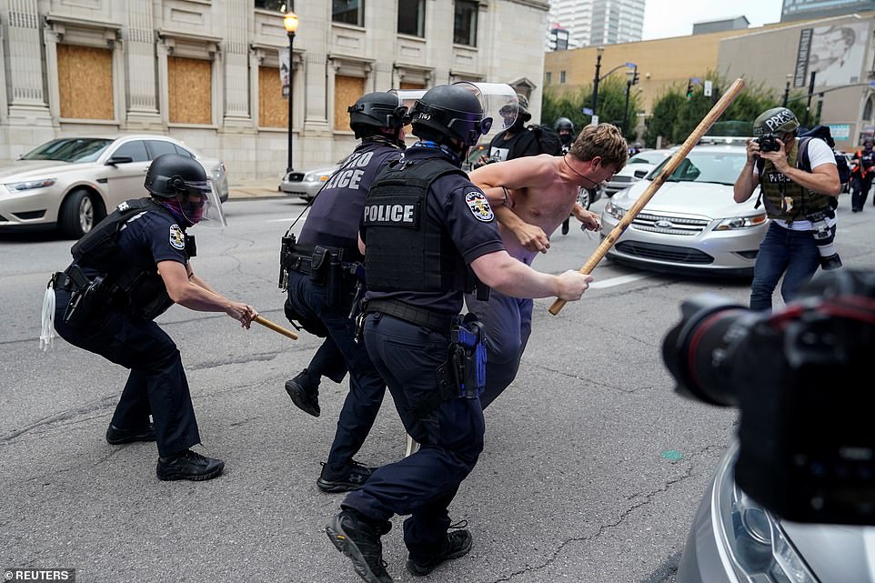 Police officers carrying batons chase down a protester during a march in downtown Louisville on Wednesday afternoon