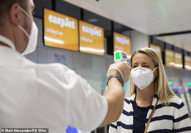 Industry leaders want ministers to commit to testing this week, with a firm timeline for implementation. Pictured: Passenger wearing face covering has temperature checked