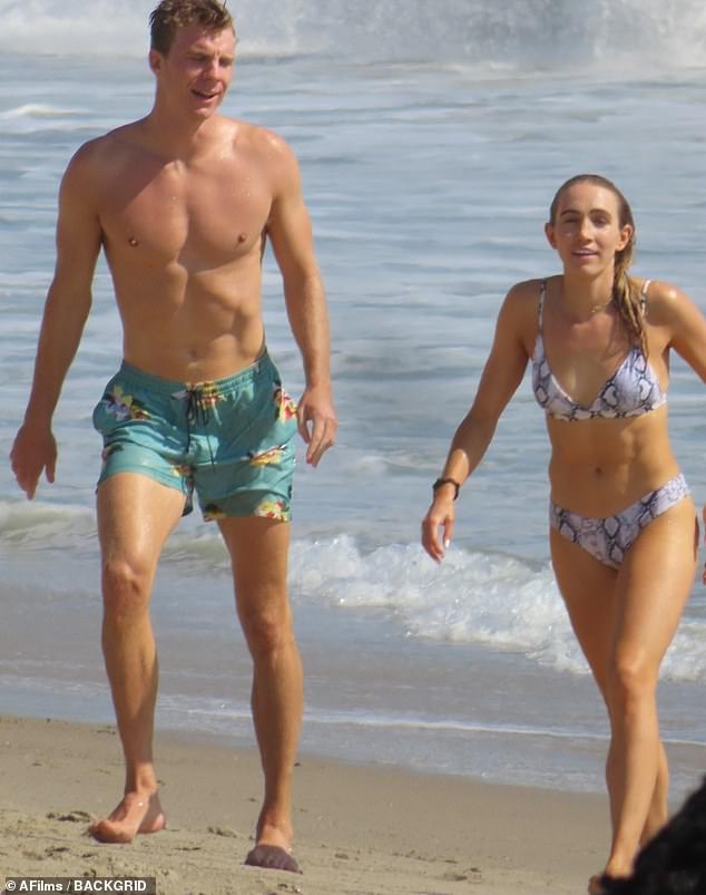Toned: Their son Nate showcased his chiseled abs in blue swim trunks as he enjoyed the ocean with a female friend