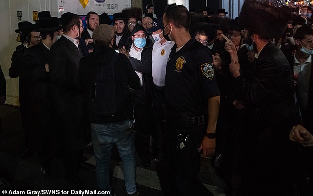 Jacob Kornbluh (hooded) is chased away and accused of being a snitch as Orthodox Jewish people gather in Borough Park