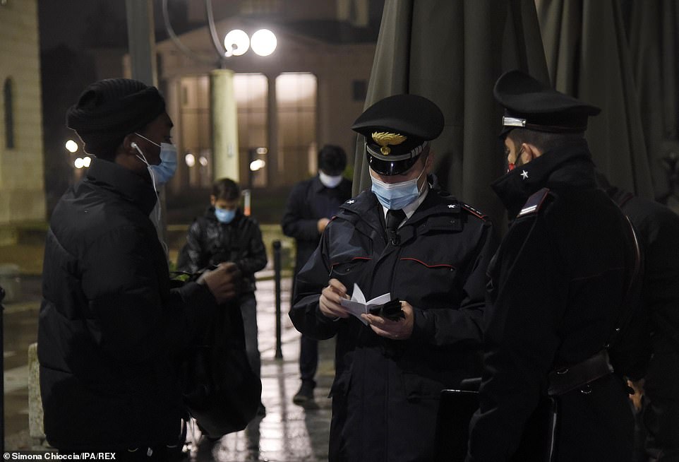 A police officer wearing a mask takes details from a passer-by, also wearing a face covering, on the streets of Milan last night