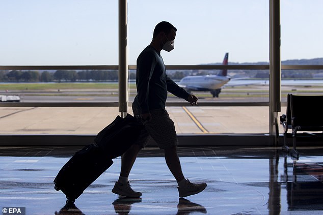 A traveler walks through a terminal as a Delta flight taxis on the tarmac behind at Ronald Reagan Washington National Airport in Arlington, Virginia