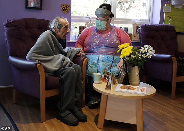 Amnesty International's report will show that Ministers 'knew from the outset' that Covid-19 posed an exceptional danger to the 400,000 residents of UK care homes, many of whom are frail and live with multiple health conditions(pictured, a nurse sitting beside a resident of Wren Hall care home in Selston)