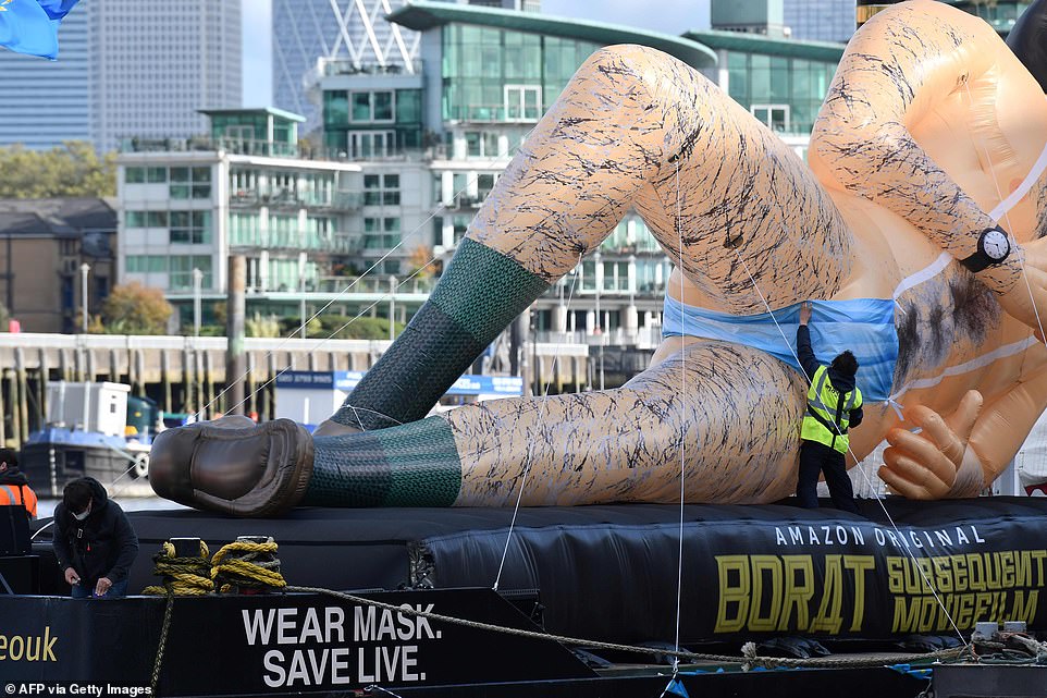 Worker ensures giant inflatable Borat is covered up as he floats down Thames to promote new movie