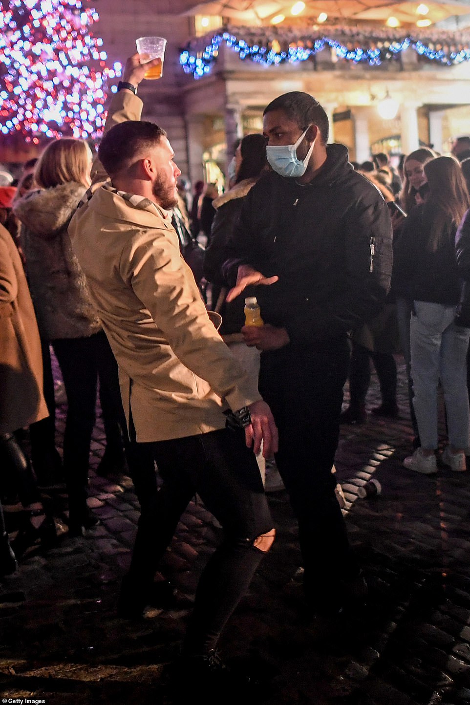 A man holding a pint dances in front of a man wearing a mask in Covent Garden in London's West End on December 5