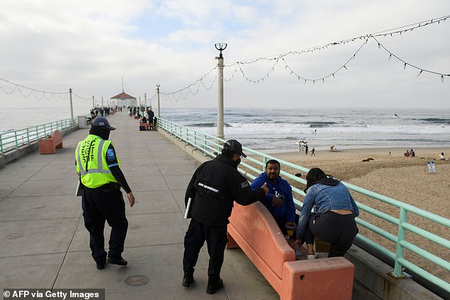 Gates signaled his support for drastic restrictions - including California Governor Gavin Newsom's latest stay-at-home order - saying: 'Bars and restaurants in most of the country will be closed as we go into this wave [of infections], and I think sadly that's appropriate.' Pictured: City workers enforce mask requirements on a pier in Manhattan Beach, California on Saturday