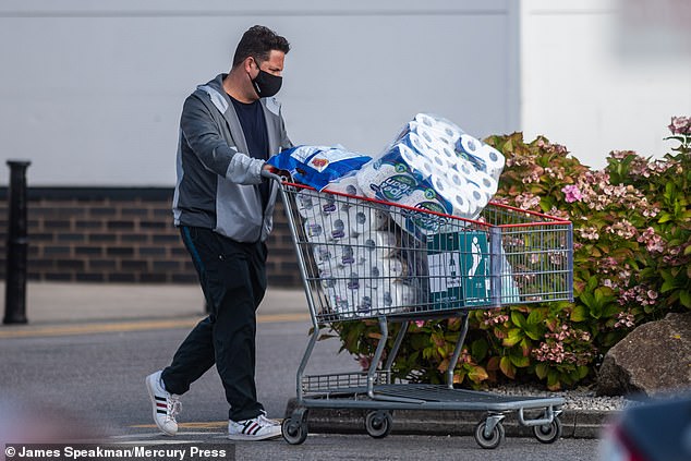 Pictured: A man leaves a Costco store in Manchester with a trolley full of toilet paper amid panic buying by people concerned about the impact of the coronavirus pandemic