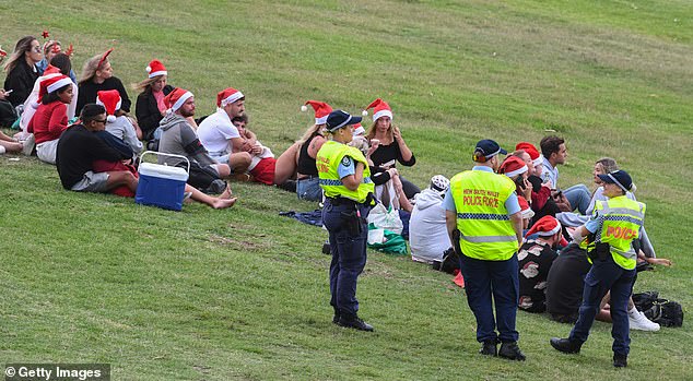 Police officers watch a group of people gathering in a large number beside Bondi Beach on December 25, 2020
