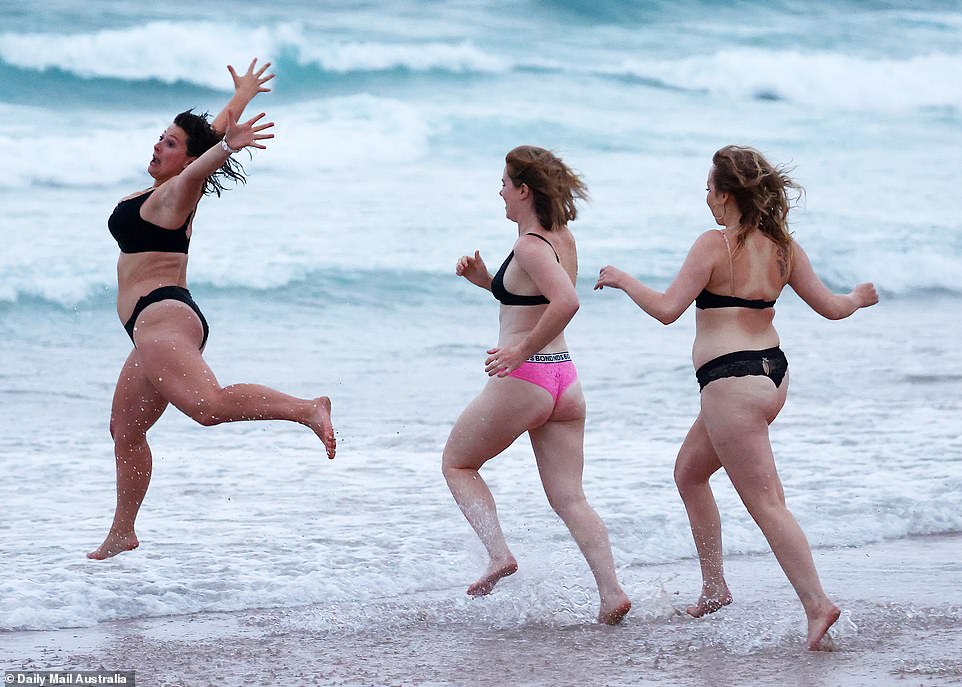 A woman jumps and throws her arms into the air as she splashes with friends at Bondi Beach on New Year's Day