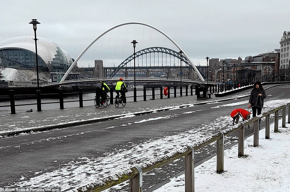 Cyclists and dog walkers pass along a snow covered Newcastle Quayside this morning following overnight snow showers