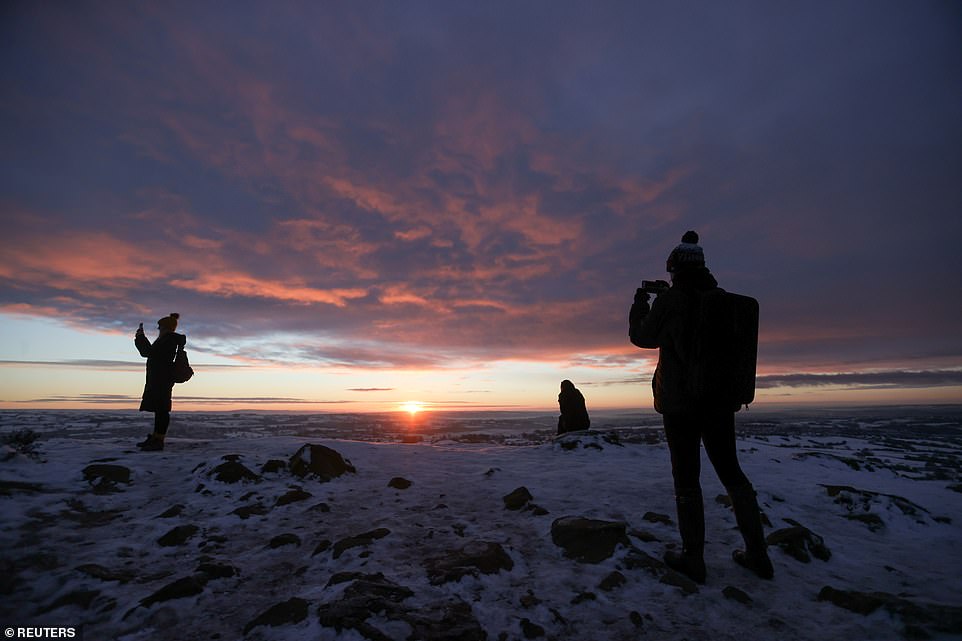 People watch the sunrise from Mow Cop Castle in Mow Cop, Britain, this morning after snowfall layered the ground