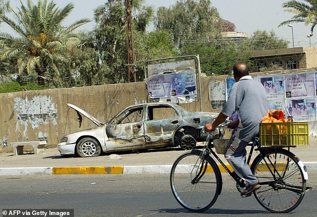 An Iraqi man rides a bicycle passing by remains of a car in Baghdad. The car was burnt during the incident when Blackwater guards escorting US embassy officials opened fire in 2007