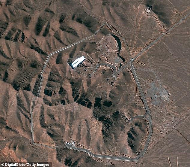 The facility is surrounded by a ring of steel and guard towers which cut through the rugged terrain - towards the top of the image a road can be seen leading inside which branches off, one route heading to a building with a white roof and another to the underground bunker