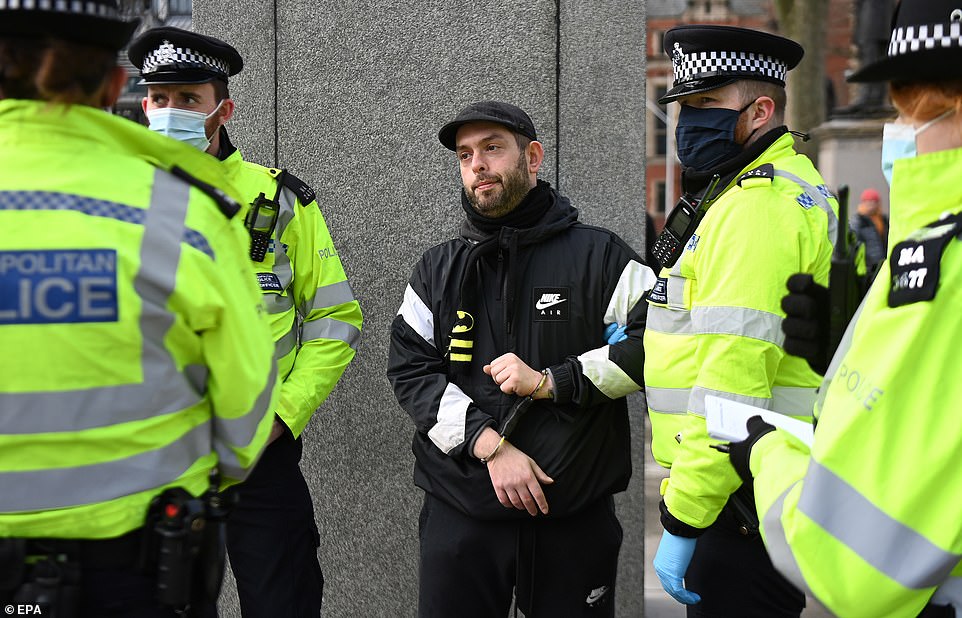 A bearded man in a cap, tracksuit and Batman scarf is put in handcuffs during an anti lockdown protest at Parliament Square