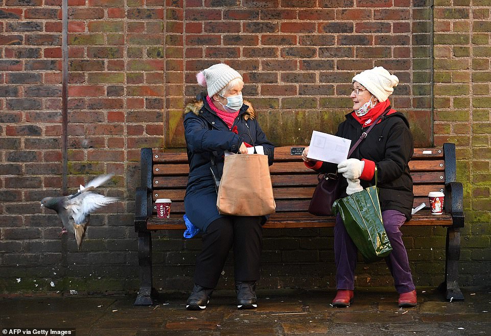 People wearing a face mask or covering due to the COVID-19 pandemic, sit and talk on a bench in York. The rules state only two people from different households can meet until April