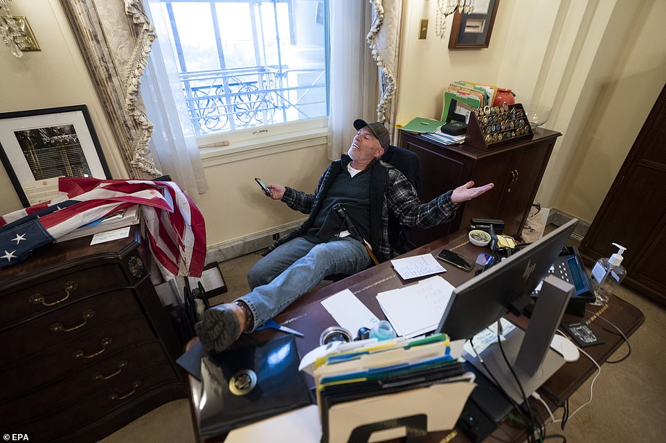 A supporter of US President Donald J. Trump sits on the desk of US House Speaker Nancy Pelosi