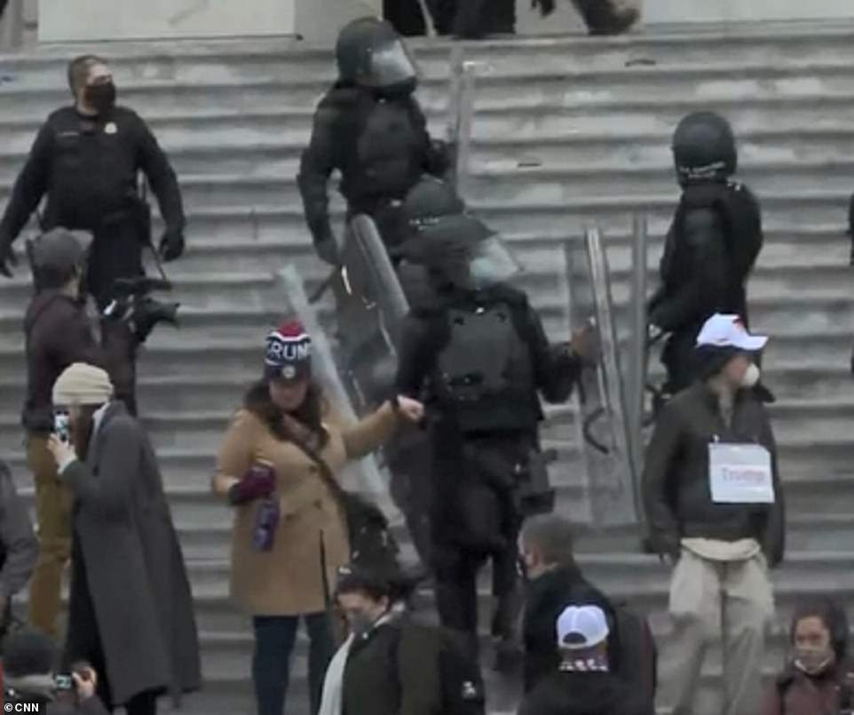 Soft touch: A Trump rioter is escorted by the hand down the steps of the Capitol Building by a cop in riot gear while others stand back and watch the chaos unfold