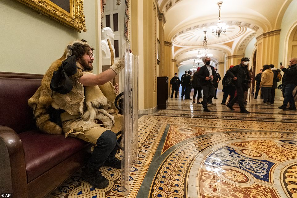 A supporters of President Donald Trump takes a seat holding a shield outside the Senate Chamber as violence erupted at the Capitol