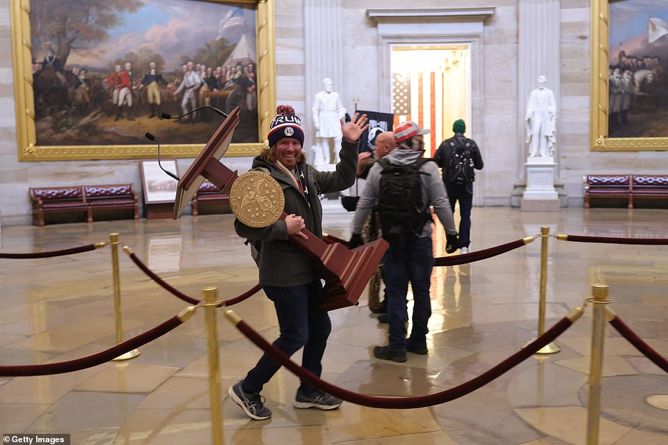 A protester walks through Congress carrying Nancy Pelosi's lectern after storming the Capitol with hundreds of others calling for Joe Biden's election to be overturned