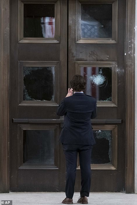 A man takes a photo of broken windows near the Rotunda in the early morning hours of Thursday