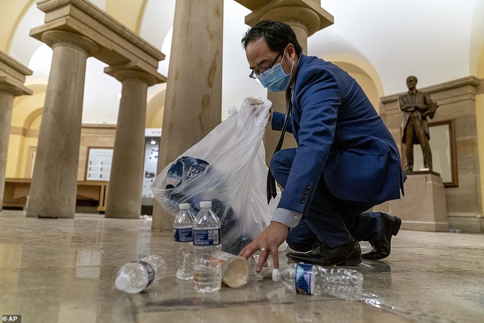 Rep. Andy Kim, D-N.J., cleans up debris and trash strewn across the floor in the early morning hours of Thursday,