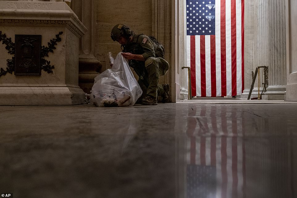 An ATF police officer cleans up debris and personal belongings strewn across the floor of the Rotunda in the early morning hours of Thursday