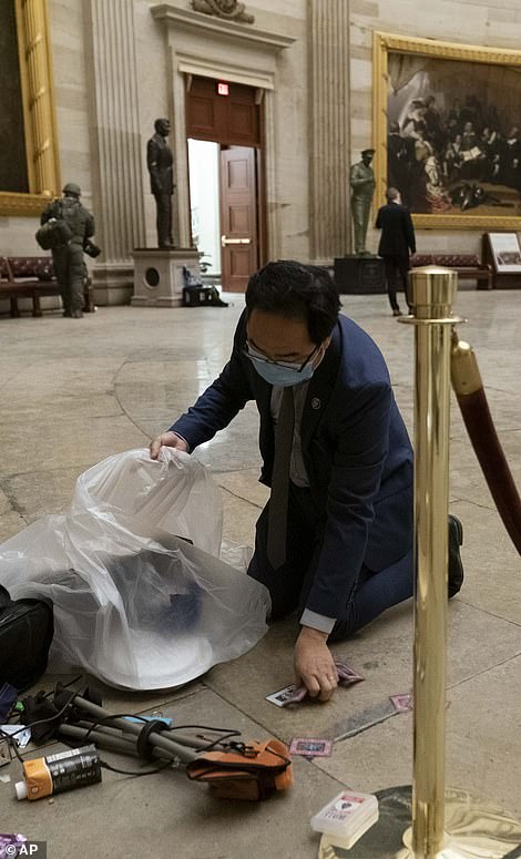 Rep. Andy Kim, D-N.J., cleans up debris and personal belongings strewn across the floor of the Rotunda in the early morning hours of Thursday