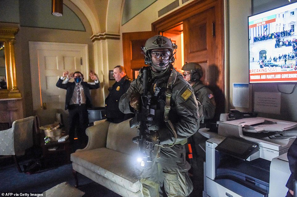 A Congressional staffer holds his hands up while Capitol Police Swat team check everyone in the room as they secure the floor of Trump supporters in Washington, DC on January 6, 2021