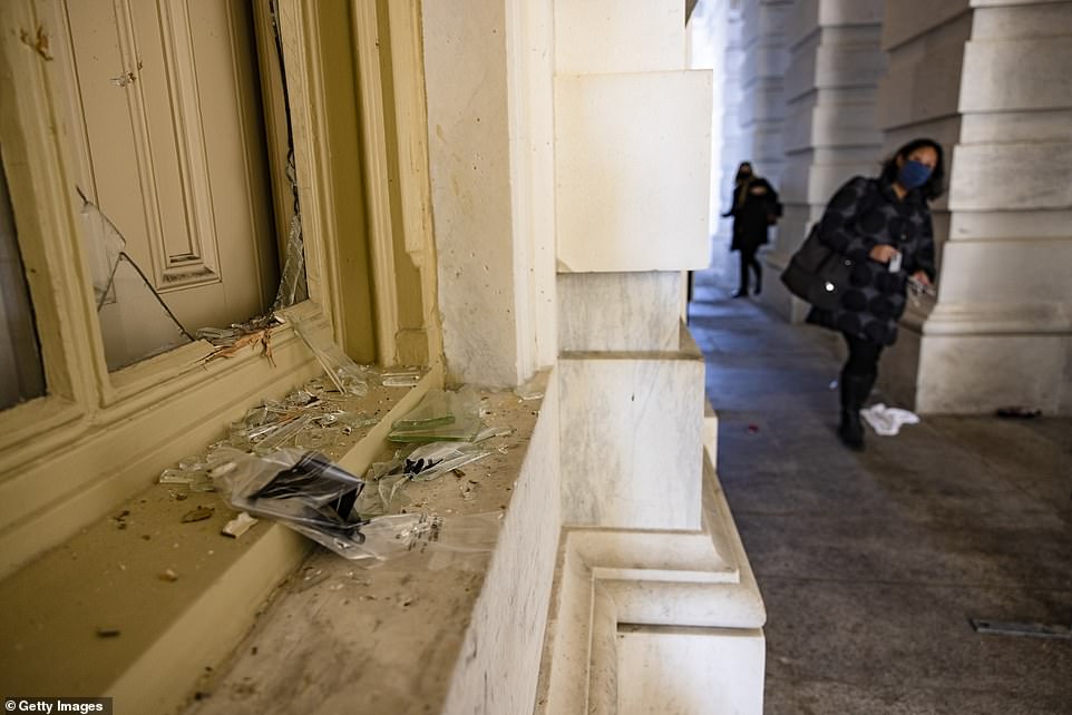 Staff walk past a shattered window next to the Senate Carriage Entrance on the eastern side of the U.S. Capitol building