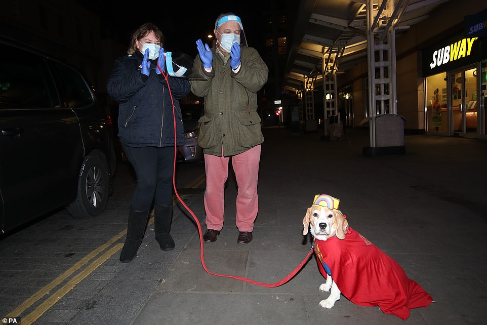 A couple stand with their dog outside the Chelsea and Westminster Hospital, London, as they join in with the applause tonight