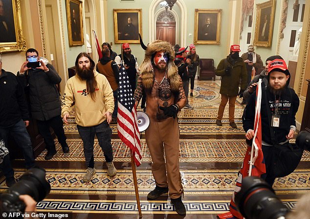 Several images of the worker, right, show him alongside the heavily-tattooed Trump supporter who sported horns, a fur hat and face paint and was named as the QAnon Shaman, or Jake Angeli, center