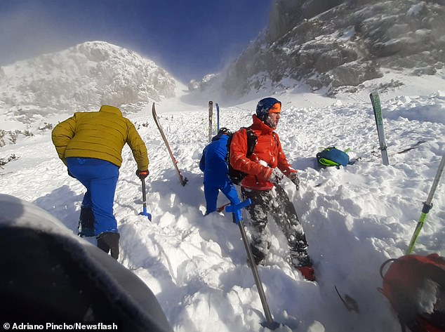 The skier who was buried (pictured in the orange jacket) was covered in snow after being rescued