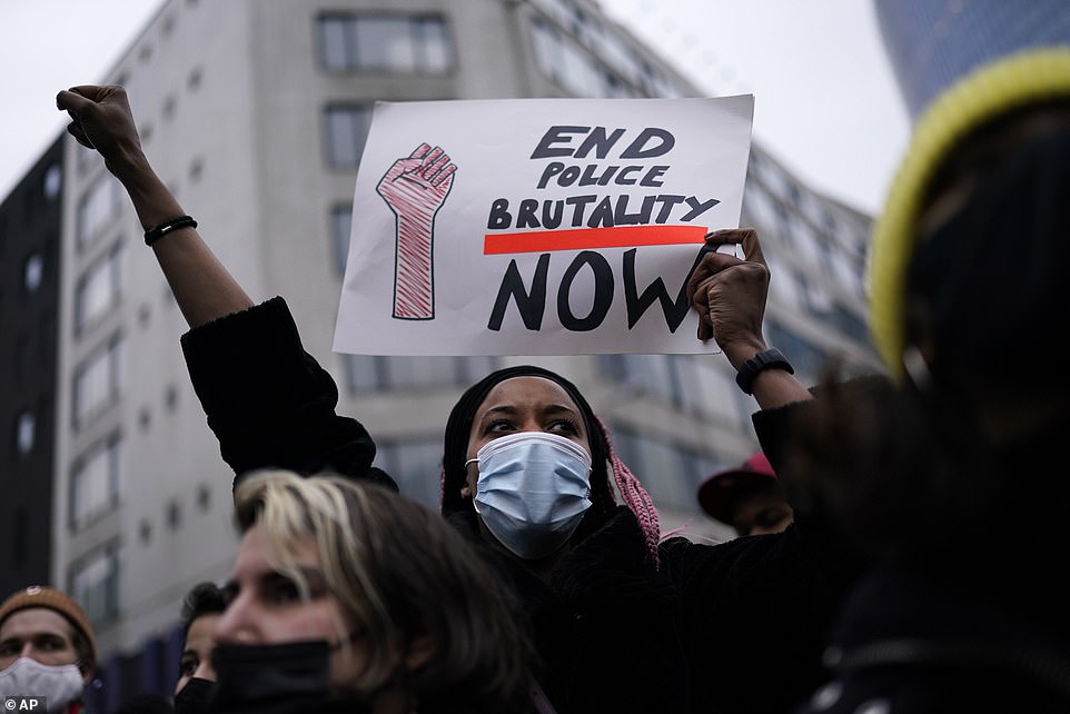 A woman wearing a face mask holds a sign that says 'End police brutality now' following the death of 23-year-old Ibrahima Barrie at the police station