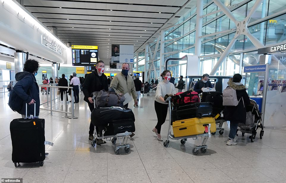 Passengers wear face masks as they walk through the international arrivals hall at Heathrow Airport's Terminal Two today