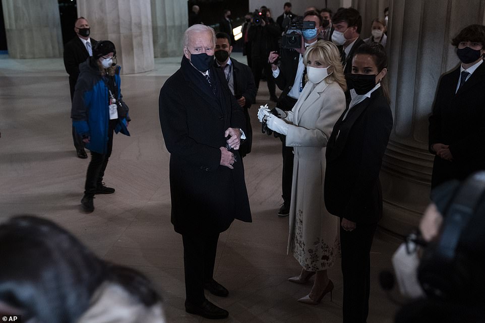 President Joe Biden adjusts his coat while first lady Jill Biden holds his gloves as they stand in the Lincoln Memorial