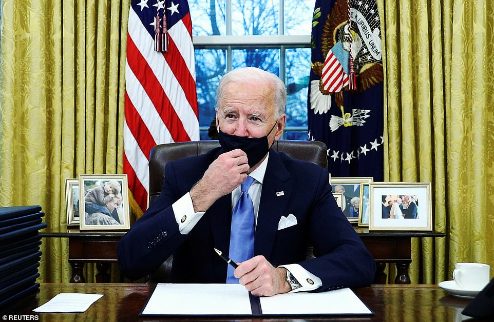 U.S. President Joe Biden adjusts his face mask as he signs executive orders in the Oval Office of the White House in Washington, after his inauguration as the 46th President of the United States. A framed picture of his late son Beau is left; a picture with his mother is second right, a picture with Pope Francis