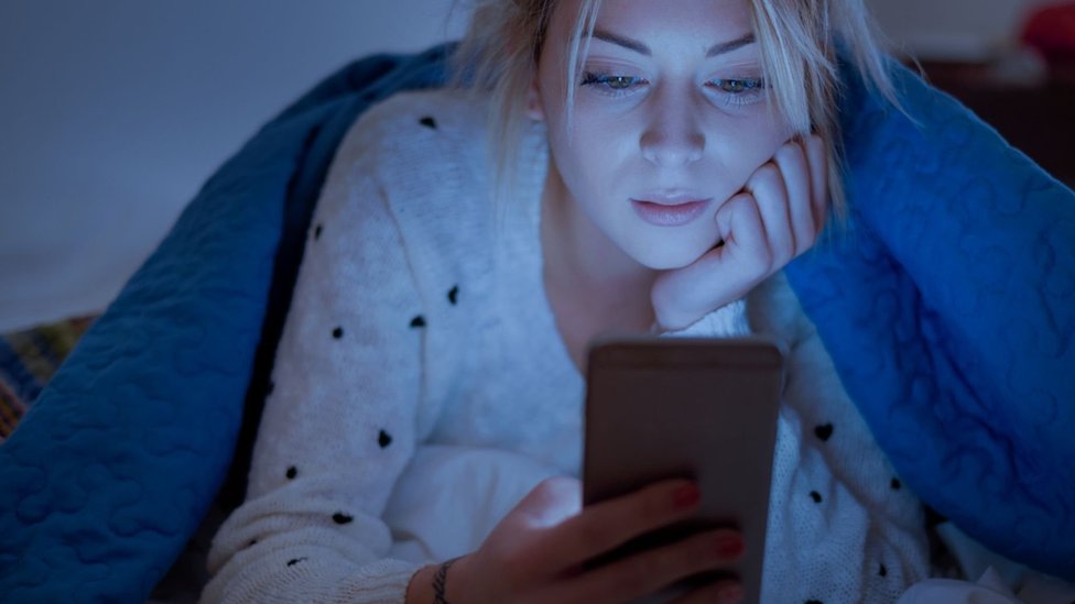 Woman with cell phone in bed.