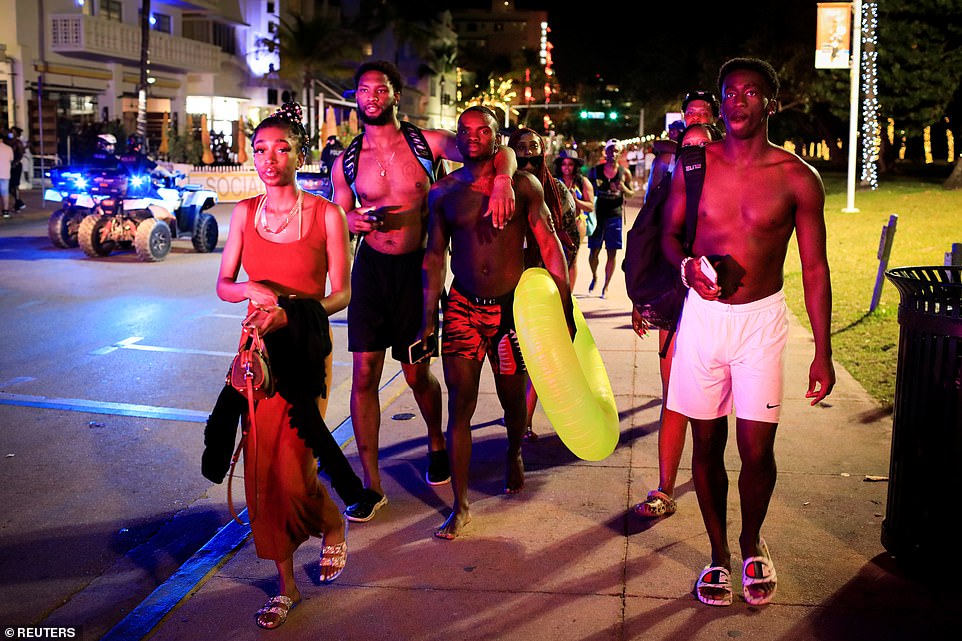 Revelers walk away as police officers ask them to leave during an 8pm curfew imposed by local authorities on spring break festivities