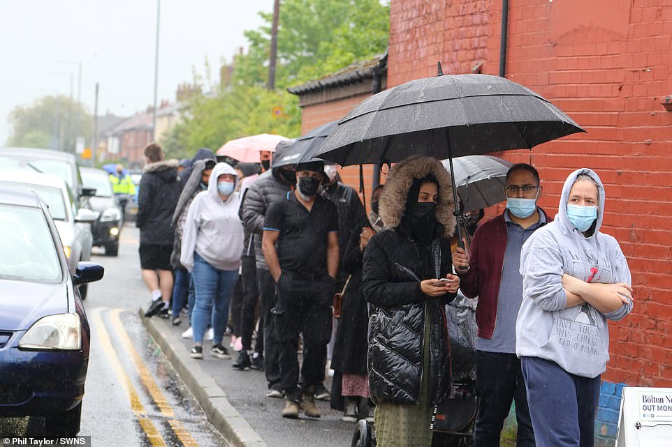 People use their umbrellas to shelter from the rain as they line up outside the pop-up centre and prepare to be vaccinated