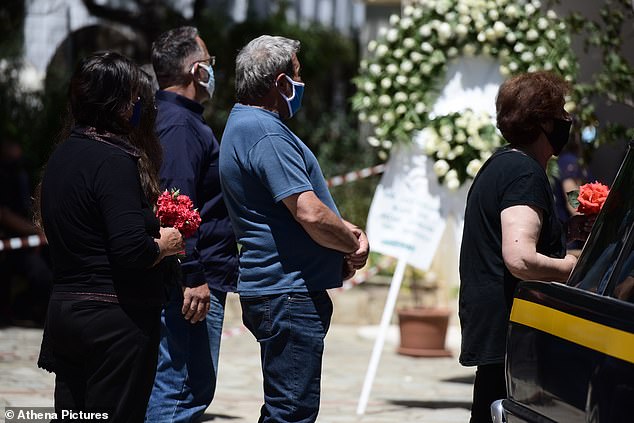 Friends and family stand next to the hearse carrying Caroline's coffin as they hold flowers outside the Agia Paraskevi church