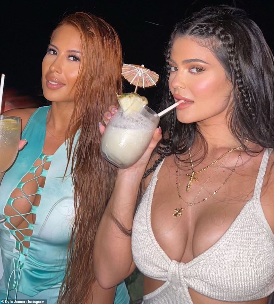 With a good pal: Here Kylie has on a beige bikini top dress with several gold chains with crosses on them as she drinks a cocktail with friend Yris Palmer