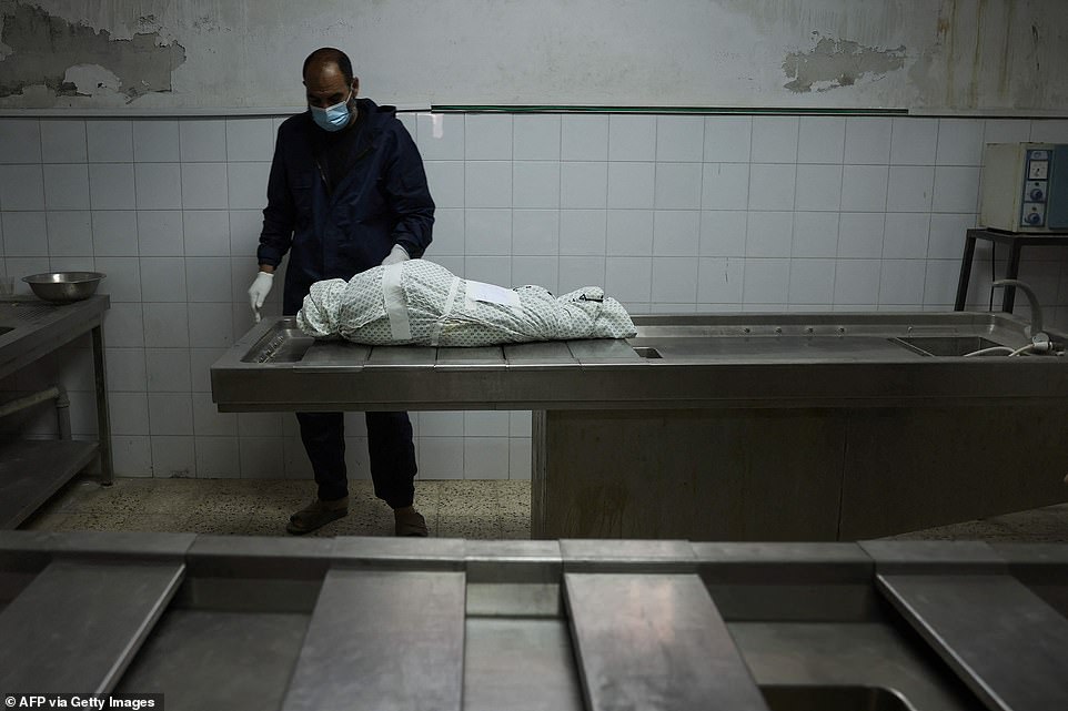 A Palestinian man stands by the body of a three year old girl killed in an airstrike on Gaza City on Wednesday