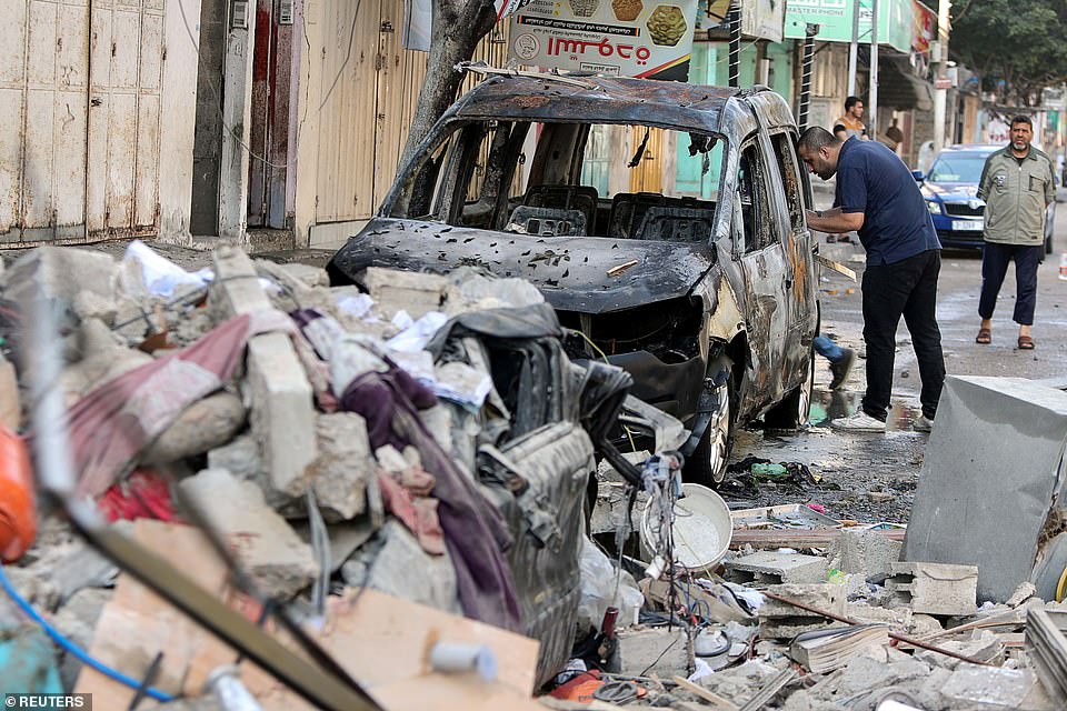 A Palestinian man inspects a damaged vehicle in the aftermath of an Israeli air strike on a house in Gaza City