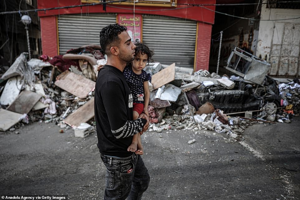 A man carrying a child passes by damaged site after Israeli army carried out airstrike over a building in the Sheikh Ridvan neighbourhood in Gaza City
