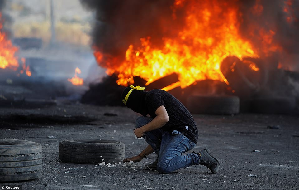 A Palestinian holds a slingshot next to burning tires during an anti-Israel protest near Hawara checkpoint, Nablus, in the Israeli-occupied West Bank, May 18
