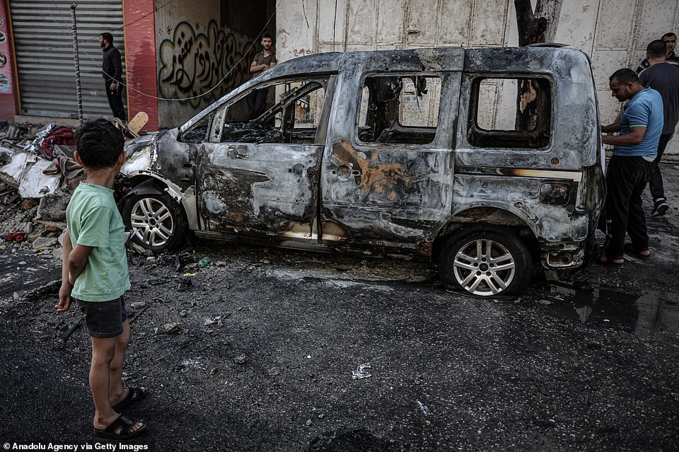 People inspect a damaged vehicle after Israeli army struck a building in the Sheikh Ridvan neighbourhood in Gaza City